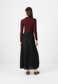 Blusa burdeos de manga larga con textura acanalada combinada con una falda larga negra; las bailarinas de punto tienen un patrón de leopardo. Texturas suaves, ajuste relajado.