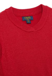 Roter gestrickter Pullover für Kinder, mit einem gerippten Rundhalsausschnitt, weichem Material und einem Etikett, das Marken- und Größeninformationen anzeigt.