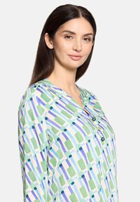 Leichtes Hemd mit Knopfleiste, das ein mehrfarbiges geometrisches Muster in Grün, Blau und Lila auf weißem Hintergrund zeigt. V-Ausschnitt, lange Ärmel.
