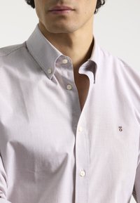 Camisa de cuadros en tonos lilas con cuello clásico, que presenta botones blancos y un pequeño logotipo bordado en el pecho.