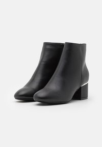 Botas de cuero negras hasta el tobillo con punta redondeada y un tacón bloque de altura media con un detalle acentuado en plata. Textura suave, diseño minimalista.