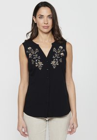 Schwarze ärmellose Bluse mit floraler Stickerei in Gold und Weiß, mit V-Ausschnitt und Knopfleiste; glattes Material mit lockerer Passform.