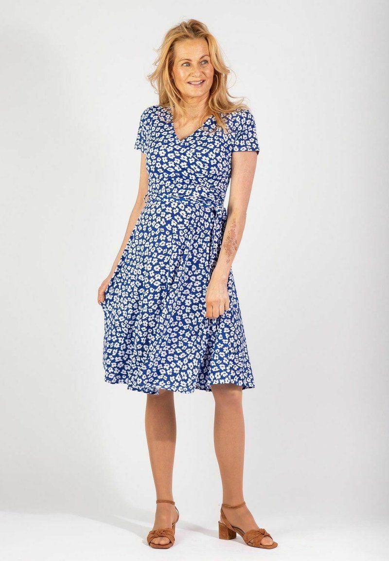 Niebieska sukienka kopertowa z krótkimi rękawami, z białym wzorem w kwiaty. Lekka tkanina z dopasowanym w pasie, delikatnie rozszerzająca się do kolan.