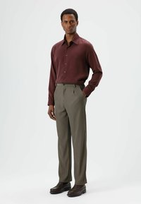 Dark red button-up shirt with a collar, paired with olive green pinstriped trousers and dark brown loafers. Smooth fabric textures throughout.