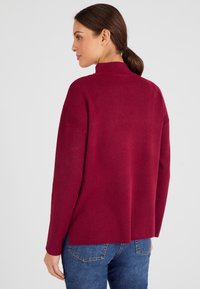 Bordeaux sweater met hoge kraag, lange mouwen en een ontspannen pasvorm. Zachte stof met een gladde textuur en subtiele stikdetails op de schouders.