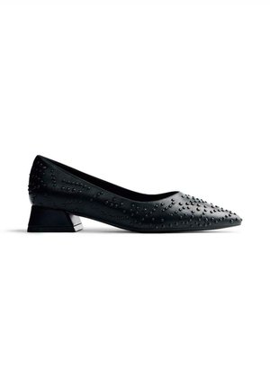 Zapato de charol negro con punta afilada, tacón pequeño de bloque y adornos de tachuelas en toda la superficie superior. Textura suave en todo.