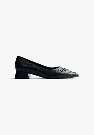 Escarpin en cuir noir à bout pointu, avec un petit talon carré et des embellissements cloutés sur la surface supérieure. Texture lisse sur l'ensemble.