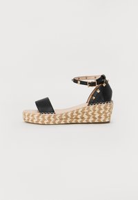 Sandale compensée en cuir noir avec bride à la cheville, accents dorés et plateforme en jute tissé présentant un motif en chevrons.