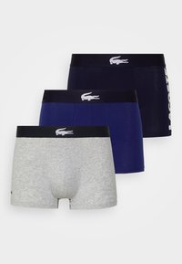 Tres pares de bóxer para hombres: uno gris, uno azul marino oscuro y uno azul marino, cada uno con una banda que presenta el logo de Lacoste en blanco.