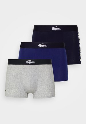 Tres pares de bóxer para hombres: uno gris, uno azul marino oscuro y uno azul marino, cada uno con una banda que presenta el logo de Lacoste en blanco.