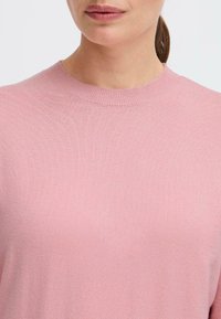 Ljusrosa stickad tröja med rund halsringning och ribbade kanter, med en mjuk textur och korta ärmar.