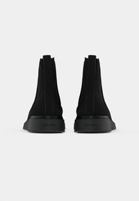 Botas pretas até ao tornozelo com parte superior em tecido liso, sola em borracha e salto elevado. Apresentam um design minimalista e a marca Calvin Klein na sola.