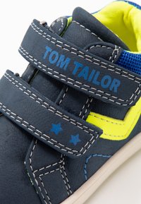 Námořnické modré boty se žlutými akcenty, suchým zipem a modrým prošíváním. Vyznačují se hvězdami na popruhu a texturovaným svrškem pro lepší úchop.