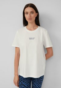 T-shirt en coton blanc avec des manches courtes, un col rond, et un texte centré qui dit : "VOTRE CORPS EST VOTRE PLUS GRAND ATOUT."