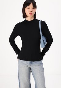 Pull noir à côtes avec des manches longues, un col haut et un corps ajusté. Associé à un jean en denim bleu clair avec des accents de couture décorative.