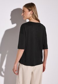 Černý krátký rukáv, volný střih, kulatý výstřih a hladká textura. Nosen s kalhotami volného střihu v neutrálních barvách.