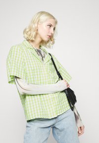 Camisa de manga curta em padrão xadrez verde e branco, acompanhada de uma bolsa preta. Tecido leve com um corte descontraído e gola pontuda.
