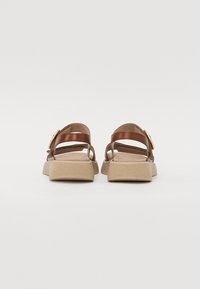 Brown leather sandals with a textured beige sole, featuring a wide strap and a buckle detail on the side. Simple and open design.