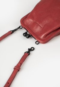 Red leather crossbody bag with a smooth texture, featuring a clasp closure and adjustable strap, complemented by black metal hardware.