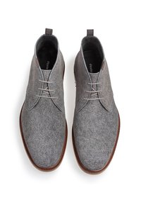 Botas de tobillo de ante gris con cordones, con un acabado liso y texturizado y una suela de cuero marrón. Presentan costuras pronunciadas y una lengüeta en el talón.