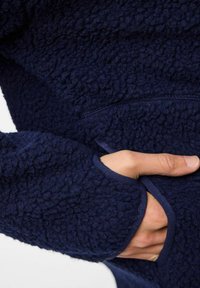 Marinblå fleecepullover med en texturerad, fluffig yta och långa ärmar, med en framficka och ribbade ärmslut.