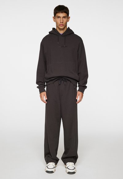 Haut à capuche gris foncé avec cordon de serrage réglable, poche avant et pantalon large assorti. Le matériau semble doux avec une texture lisse.