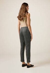 Pantalons gris à carreaux avec une coupe ajustée et une cheville fuselée. Le matériau semble texturé, associé à un haut sans manches beige et des chaussures noires.