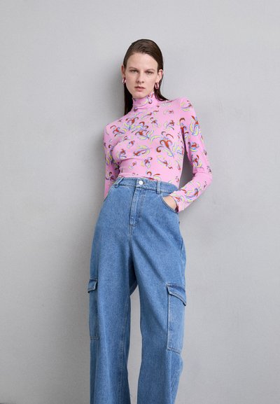 Aansluitend roze langemouwen shirt met veelkleurige spiraalpatronen, gecombineerd met losse blauwe denim cargo pants met zijzakken. Neutrale achtergrond.