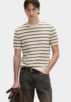 Roomkleurige korte mouwen trui met donkere horizontale strepen, ronde halslijn en geribde zoom. Gecombineerd met donkere spijkerbroek en een gevlochten riem.