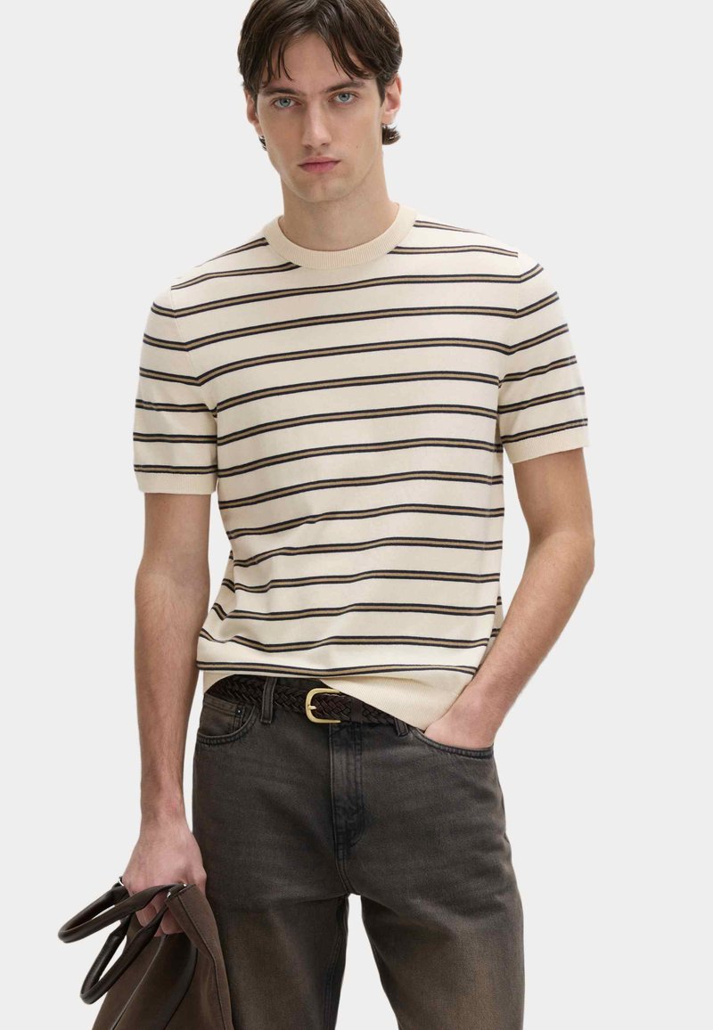 Flødefarvet strik top med korte ærmer og mørke horisontale striber, rund halsudskæring og ribkant. Kombineret med mørke jeans og et flettet bælte.