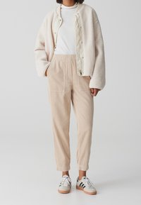 Cream teddy bomber jacket, white long-sleeve top, beige corduroy pants, and grey with black stripes sneakers. Soft textures and relaxed fit.