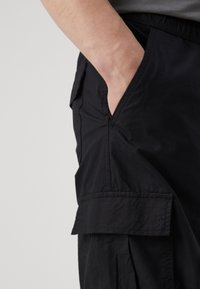 Czarne spodnie cargo z boczną kieszenią i luźnym krojem. Wykonane z lekkiego materiału z widocznymi szwami i gładką fakturą.