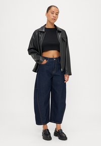 Jachetă de piele sintetică neagră, top negru scurt, blugi denim cu talie înaltă și croială largă, cu tivuri ușor contrastante, și pantofi cu platformă negri.