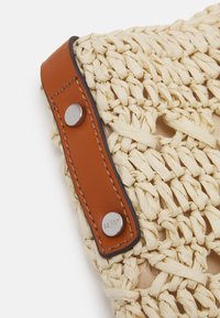 Geweven rieten handtas met beige en lichtbruine draden, voorzien van een bruine leren riem die vastzit met metalen klinknagels. Minimalistisch ontwerp, open geweven patroon.