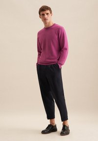 Maglione a girocollo magenta in maglia abbinato a pantaloni larghi scuri e scarpe in pelle nere. Texture liscia, design semplice, vestibilità casual.