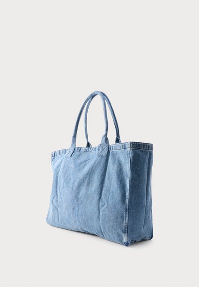 Lichtblauwe denim draagtas met twee schouderriemen, rechtopstaand op een eenvoudige lichtgrijze achtergrond.