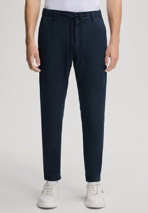Pantaloni blu navy con vita regolabile e tasche anteriori, realizzati in tessuto leggero. Indossati con scarpe da ginnastica bianche su uno sfondo neutro.