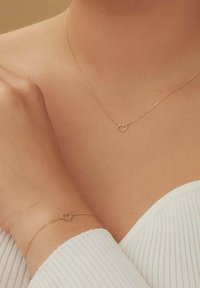 Goudkleurige ketting en armband met kleine hartvormige accenten. Fijne kettingstructuur. Eenvoudig, minimalistisch ontwerp dat geschikt is voor het opstapelen.