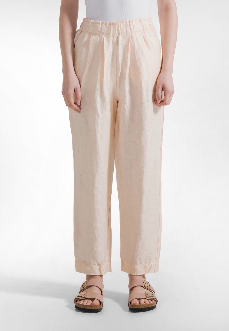 Løse hørbukser i ferskenfarve med elastik i taljen og manchetter ved anklerne, lavet af et blødt, tekstureret stof.