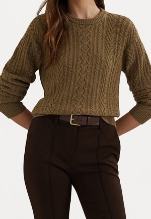 Femme portant un pull en maille torsadée marron, rentré dans un pantalon taille haute marron foncé avec une ceinture assortie à boucle dorée.