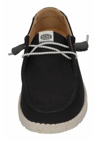 Black canvas slip-on shoe with a textured design, white speckled rubber sole, and contrasting white laces. Label reads "HEY DUDE."