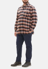 Karierte Flanellshirt in Navy, Orange und Weiß; mit Knopfleiste und Brusttasche. Kombiniert mit navy Bl trousers und dunklen Stiefeln.