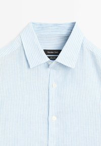 Light blue linen shirt with vertical white stripes, a pointed collar, and a front placket featuring white buttons. Brand label visible.