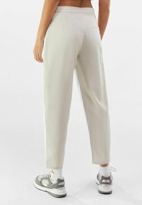 Pantalones de raya diplomática en gris claro con un corte relajado, que cuentan con un bolsillo trasero y una textura suave. Combinados con zapatillas grises y calcetines blancos.