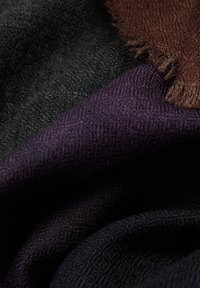 Textiel met zwarte, donkerpaarse en bruine materialen; heeft een zachte textuur met een subtiel patroon en rafelige randen.