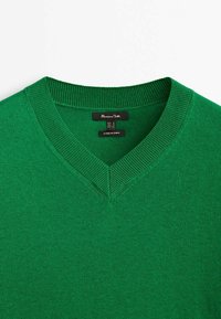 Vihreä neulepaita, jossa on V-pääntie ja ribbineulospäät. Pehmeä rakenne, jossa on tasainen väri, varustettu merkkitiedoilla ja kokotiedoilla.