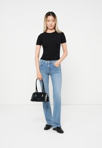 Black short-sleeve top, light blue flared jeans, black handbag with two handles, black shoes, standing against a plain white background.