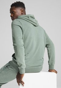 Sudadera de algodón verde claro con un acabado texturizado y capucha con cordón. Presenta puños y dobladillo acanalados, acompañados de joggers a juego.