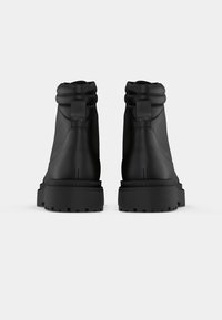 Fekete bokacsizmák sima, matt textúrával, vastag gumitalppal és hajtott gallér dizájnnal. Minimalista fém alkatrészek jellemzik, és letisztult sziluettet mutatnak.