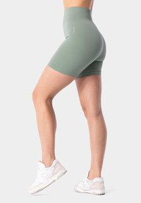 Hoge taille, olijfgroene shorts van rekbare stof, met een gladde textuur en subtiele ontwerpdetails. Draagt met witte sneakers.